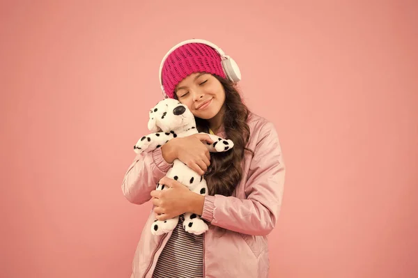 Я так тебе кохаю. щаслива маленька дівчинка грає в іграшку для собак. рожевий - її улюблений колір. маленька дитина слухає музичні навушники. дитина довге кучеряве волосся. затишний зимовий сезон. догляд за тваринами. теплий одяг для холодної погоди — стокове фото