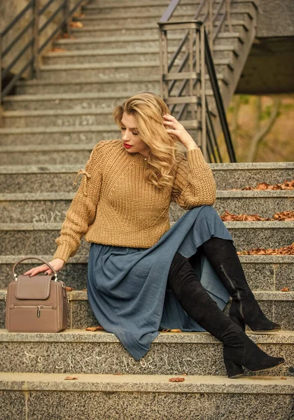 Fall fashion trend. Wearable trends. Layer oversize knit over girly skirt. Fall outfit formula. Style Sweater and Skirt Combo for Fall. Woman gorgeous hairstyle sit on stairs outdoors. Warm autumn