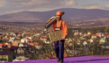İşini çok seviyor. Özel koruma giysisi içinde çatı tamircisi. İnşaat binasının altındaki yeni çatı. İnşaatçılar çatı keçesi kullanır. Profesyonel tamir çatısı. Düz çatı kurulumu