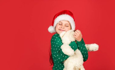 Oyuncak ayı. Noel titreşimleri. Kutup ayısı. Noel hediyesi alışverişi. Noel tatili. Kış neşeli mevsim. Xmas alışverişi. Oyuncaklı küçük Noel Baba. Küçük kız Noel Baba kırmızı arka plan