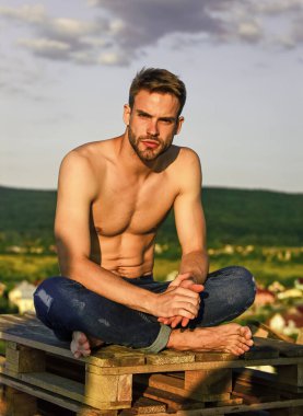 Eğitimden sonra dinleniyorum. Kot pantolon giymiş seksi bir adam. Gökyüzü arka planında erkek manken. Yaz, açık havada dinlenmek. Sporcunun seksi bir vücudu var. Gün batımında kaslı bir adam. Maço adamın çıplak gövdesi vardır.