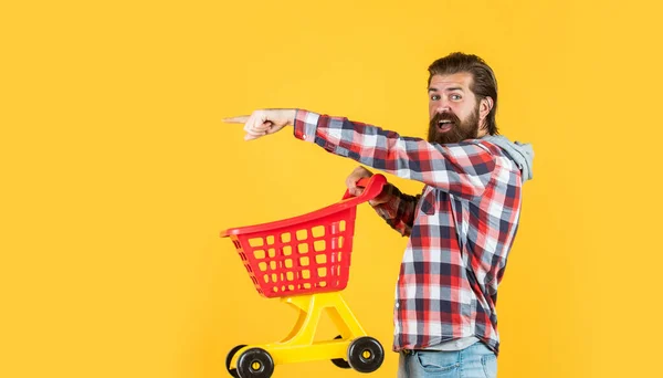 Dia de compras bem sucedido. Comprador masculino com carrinho de compras. O tipo barbudo de camisa quadriculada compra. homem brutal sem barba com barba. comprar produtos no shopping. deveres cotidianos e rotina — Fotografia de Stock