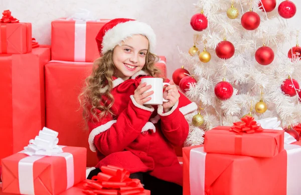 Dziewczynka małe urocze dziecko trzymać kubek z gorącym napojem podczas świętowania Bożego Narodzenia. Gorący napój kakaowy w Wigilię. Ulubiony napój kakaowy. Kapelusz Mikołaja lubi gorący napój. Pyszne ciepłe napoje dla dzieci — Zdjęcie stockowe