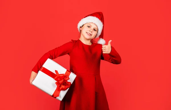 Gift package. Promotional purposes. Give away. Merry Christmas and happy holidays. Winter holidays. Little girl Santa hat hold gift box. Kid hold present box red background. Xmas gift shopping