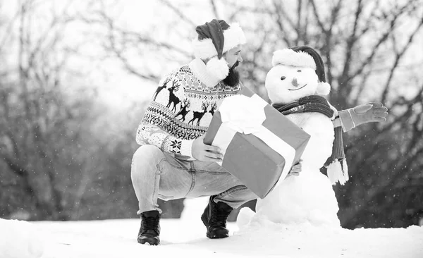 Posando para la foto. vacaciones de invierno. suéter caliente en clima frío. hombre barbudo construir muñeco de nieve. Feliz año nuevo. hipster feliz listo para Navidad. temporada de invierno. Feliz navidad. hombre de santa dar regalo al aire libre — Foto de Stock