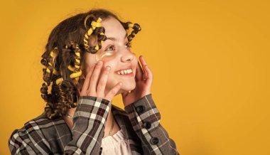 Göz bantlı mutlu çocuk. Saçlarının etrafında kıvırcık kızlar. Güzel bir saç stili yap. Harika bir saç stili. Kuaför salonu. Sarı arka planda saçları tokalı ve bigudili bir kız.