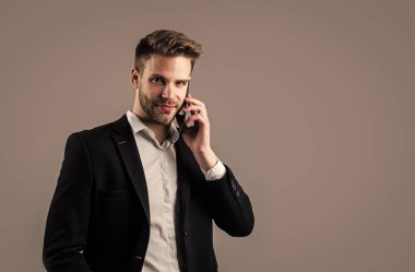 Kendine güvenen iş adamı akıllı telefon kullanır. Cep telefonlu patron erkek. Gri arka planda seksi CEO. Modern ofis hayatı. Karizmatik iş sahibi. Şık simsar. Takım elbiseli yakışıklı adam. Boşluğu kopyala