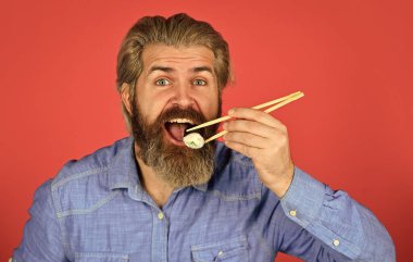 Suşi ruloları. Japon mutfağı. Asya yemeği. Suşi siparişi. Adam evde suşi yiyor. Çubuklu suşi ve zencefil. Doğu kültürü. Sakallı hippi rulo yiyor. Japon yemek servisi.