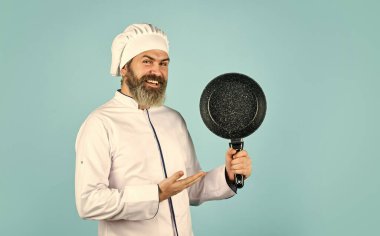 Profesyonel mutfak gereçleri. Teflon zehirli olabilir. Kızartma için yapışmaz tava. Tereyağından kıl çeker gibi. Adam tavayı tutar. Kızartma yemeği. Sağlıklı yiyecekler. Sakallı şef kahvaltı hazırlıyor. Yağsız kızarma