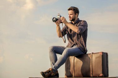 Seyahat blogu. Adam bavula oturur. Yakışıklı gezgin geçmişe dönük kamera. Klasik valizli bir adam. Fotomuhabir konsepti. Bagajla seyahat et. Gezgin blogcu. Video bloğu çekiliyor. Tatil zamanı.