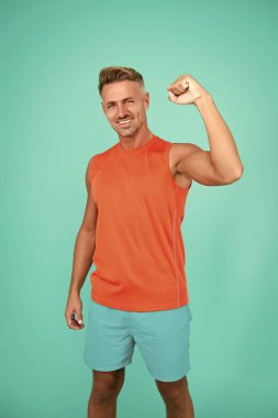 Atletik gücünü arttır. Mutlu adam mavi arka planı düzeltir. Formda olan adam kas gücünü gösteriyor. Spor kıyafetleri ve spor giysileri. Güç ve güç. Güç için antrenman. Spor ve spor