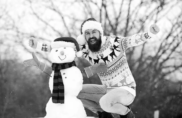 Een bebaarde man bouwt sneeuwpoppen. Gelukkige hipster klaar om Kerstmis te vieren. winterseizoen activiteit. man santa hoed spelen met sneeuw. wintervakantie buiten. warme trui bij koud weer. het kerstfeest — Stockfoto