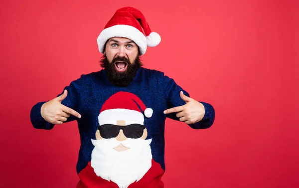 Жестокий бородатый парень в шляпе Санты Клауса и свитере на Рождество, реклама — стоковое фото