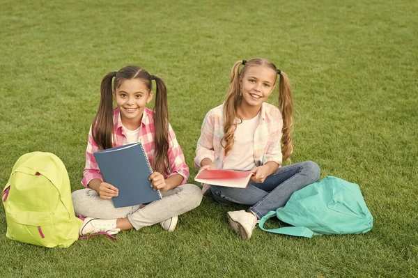 知识的日子来了。在绿草上玩得开心。两个背着背包的小孩。小女孩在课间休息时玩耍和学习。孩子们快乐的一天。姐妹关系和家庭观念。夏天快乐 — 图库照片