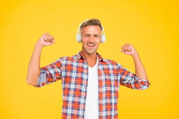 Happy man flex brazos fuertes escuchando música en los auriculares modernos fondo amarillo, potencia de sonido — Foto de Stock