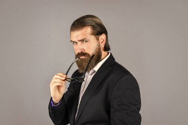 Erkek ceketi dolabı. Modaya uygun bir adam gözlük takıyor. Resmi manken. Gri arka planda duran yakışıklı adam. Ciddi sakallı iş adamı. Modern görünümlü şık, olgun bir adam. Mükemmel erkek.