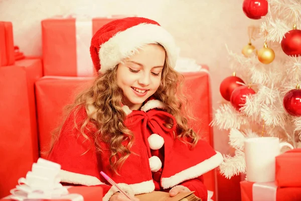 O traje do Pai Natal acredita em milagre. Carta para o Pai Natal. Lista de desejos. Menina criança segurar caneta e papel perto de árvore de natal escrevendo carta. Fui boa rapariga o ano todo. Criança escrever carta para santa claus — Fotografia de Stock