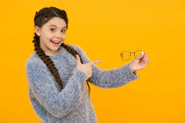 노란 배경 과 건강 보험에 관한 안경을 손가락으로 가리키는 멋진 머리를 한 소녀가 웃고 있습니다. — 스톡 사진
