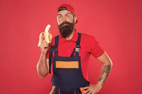 Viver uma vida saudável. Conceito saboroso e saboroso. Morde banana. Um faz-tudo com fome. Faça um lanche saudável. Homem barbudo de uniforme e gorro comendo banana. Trabalhador construtor mecânico comer banana. Frutas frescas — Fotografia de Stock