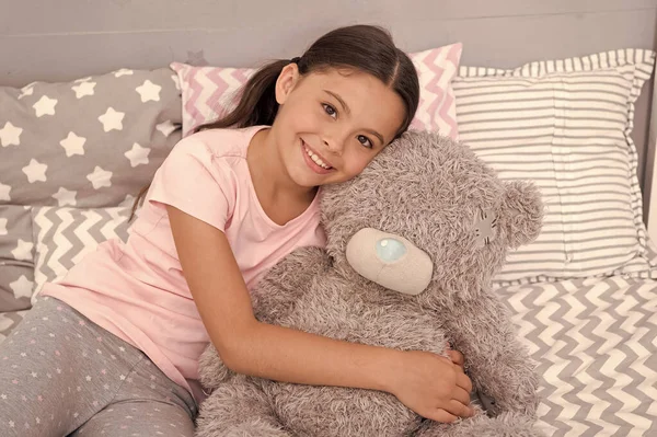 Kids evening routines. Favorite toy. Girl child hug teddy bear in her bedroom. Pleasant time in cozy bedroom. Girl kid long hair cute pajamas relax and play plush teddy bear toy. Pure love concept. — Stock Photo, Image