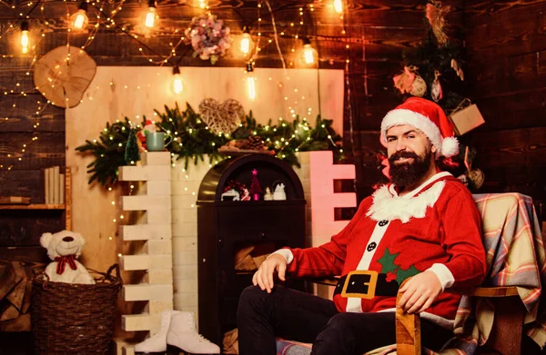 Vacaciones de invierno. Saludos desde Santa. Querido Santa. Residencia de Santa Claus. Ambiente acogedor en casa. Decoraciones de invierno. Concepto de oficina de Santa Claus. barbudo hipster hombre sentarse en sillón cerca de la chimenea — Foto de Stock