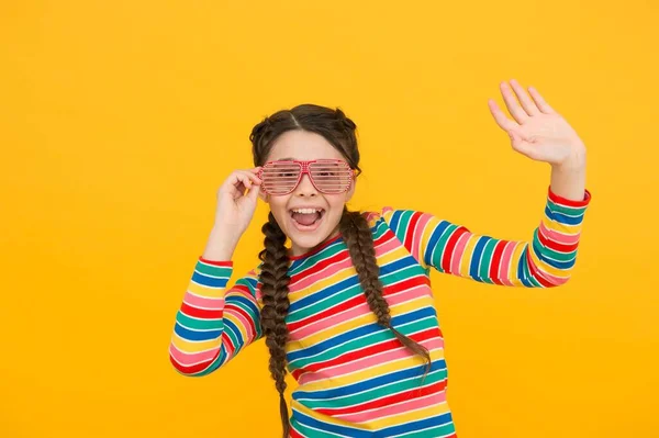 Bambino felice ragazza con capelli intrecciati usura arcobaleno colore e glamour occhiali da festa su sfondo giallo, infanzia felice — Foto Stock