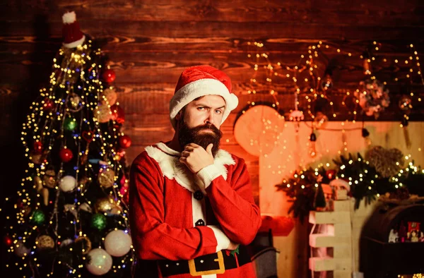 Thoughtful Santa claus. Winter holidays. Cozy home atmosphere. Winter decorations. Santa Claus bearded hipster serious pensive face man defocused garland lights background. Santa thinking about gifts