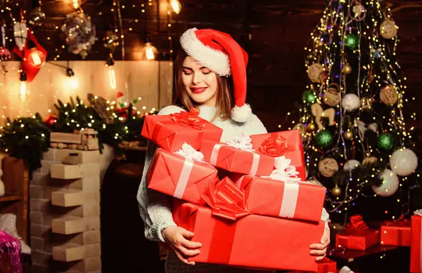 Принеси магію комусь життя. Пані Санта святкує Різдво вдома. Дівчина стильний макіяж червоних губ тримає багато різдвяних подарунків. Затишна різдвяна атмосфера. Жінка Санта Клаус капелюх напередодні Різдва — стокове фото