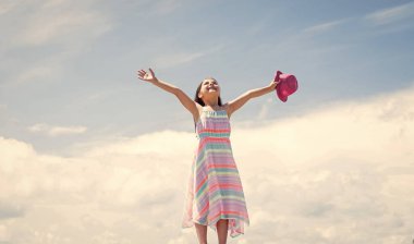 Harika bir tarzı var. Küçük kızın uzun gür saçları var. Elbiseli çocuk. Kadın kuaför salonu. Güzellik ve yaz modası. Gökyüzü arka planındaki neşeli çocuk. Modayı takip eden bir çocuk. Mutlu çocukluk