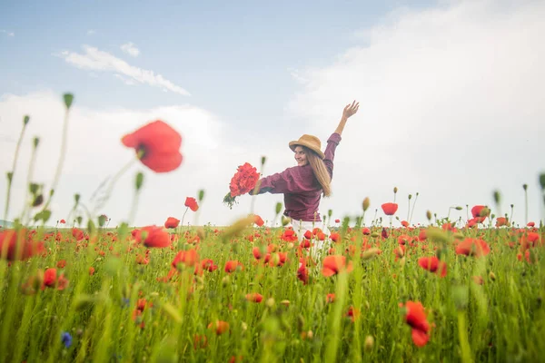 Lovely atmosphere. seasonal beauty landscape. young girl in hat walk in meadow. vacation. sense of freedom. beautiful woman gather red poppy flower bouquet in field. summer or spring nature