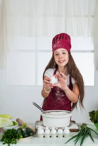 집안일과 집안일을 돕는 일. 아동 발달. 부엌에서 굽는 작은 소녀. 아이 요리사가 반죽을 만들고 있습니다. 아이들은 집에서 건강에 좋은 음식을 준비하고 요리용 유니폼을 입습니다. 진짜 맛있는 음식 — 스톡 사진