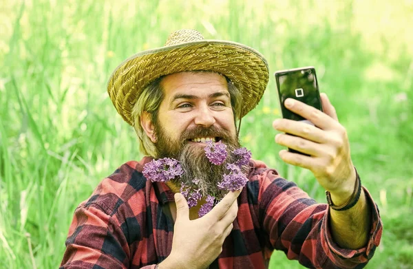 Emoções puras. selfie verão com lilás no telefone. rancho hipster tem longa barba saudável. flor no cabelo. agricultor relaxado em chapéu de palha. homem maduro jardineiro relaxar na grama verde. desfrutar de natureza primavera — Fotografia de Stock