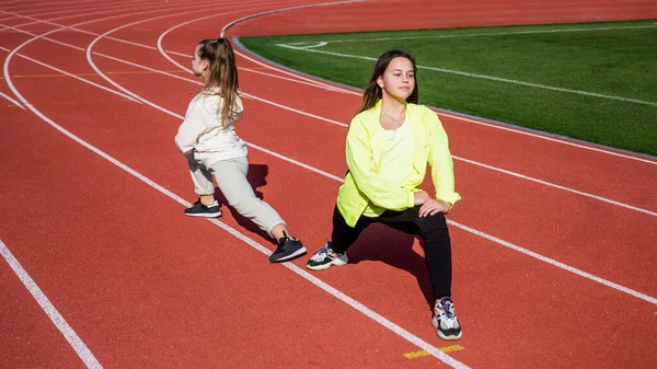 Meninas adolescentes que se alongam antes da maratona de corrida. corredores se preparam para competição de corrida. sprinter aquecendo no ginásio do estádio. flexibilidade. treinamento de crianças na escola aula de educação física — Fotografia de Stock