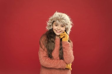 Çocuk gülümsemesi kırmızı arka plan. Yumuşak tüylü aksesuar. Kış mevsimi. Küçük moda anlayışı. Çok rahat hissediyorum. Çocuk uzun saçlı yumuşak şapkalı. Kış moda konsepti. Soğuk kış havası için sıcak şapka