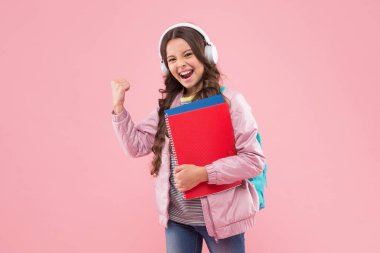 Kulaklıklı mutlu çocuk okul kitaplarını tutuyor enerjik kol hareketleri yapıyor pembe arka plan, ses gücü
