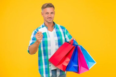 Elinde paketler olan mutlu yakışıklı adam tatile hazırlanıyor ve kredi kartı gösteriyor, yeni yıl tebrikleri.