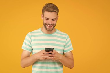 SMS mesajı gönderiliyor. Mutlu adam SMS 'i akıllı telefon sarı arka planıyla gönderiyor. SMS mesajı. Kısa mesaj servisi. Yeni teknoloji. Taşınabilir yaşam tarzı. Modern hayat. Güvenilir SMS teslimatı