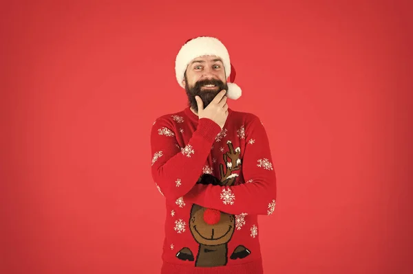 Coś mu chodzi po głowie. Zimowe wakacje. Człowiek brodaty hipster nosi czapkę z dzianiny zimowej. Fryzjer na twarzy. Zimowa moda. Facet w zimowych ciuchach. Brodaty Santa Claus czerwone tło — Zdjęcie stockowe