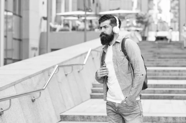 Voyagez gratuitement avec la technologie. Homme barbu écouter de la musique urbaine en plein air. Hipster porter des écouteurs dans un style décontracté. Nouvelle technologie. Technologie sans fil. La vie moderne. Garder les oreilles en sécurité grâce à la technologie — Photo