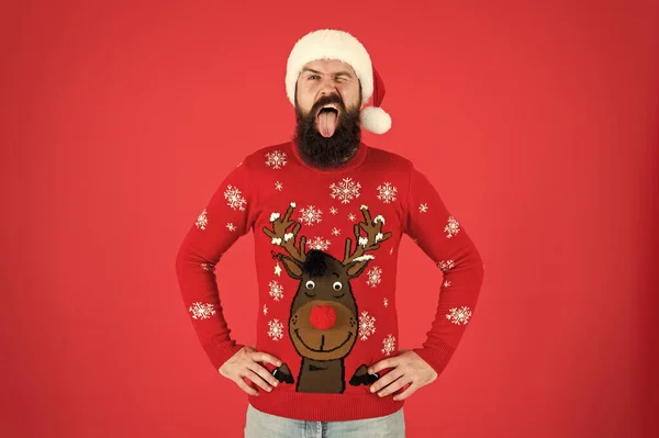 Merry christmas. ready for xmas party. happy new year. winking hipster funny knitted sweater. warm clothes in cold winter weather. holiday season mood. bearded man santa hat red background. — Stock Photo, Image