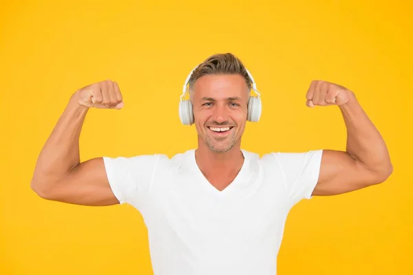 Hanki voimakkaita ääniä. Vahva mies taivuttaa käsivarret keltainen tausta. Kuulokkeiden teknologia. Moderni harjoitus ja koulutus. Voima ja voima. Vahva musiikkikokemus — kuvapankkivalokuva