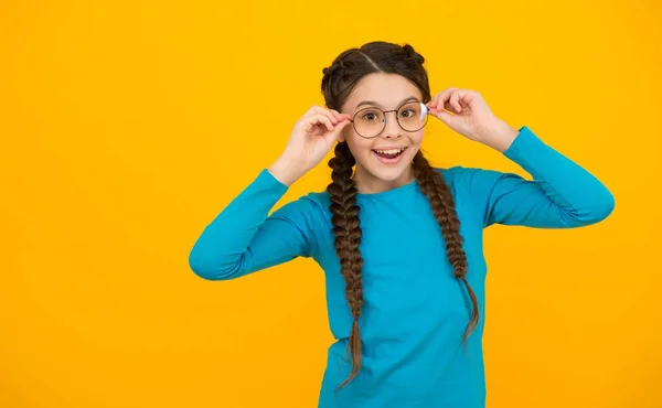 Menina feliz em óculos para a visão tem penteado na moda no fundo amarelo, escola — Fotografia de Stock