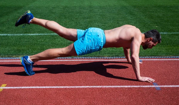 Hombre haciendo ejercicios de flexiones en el estadio. gimnasio gimnasio al aire libre. musculoso atlético. Deporte. fuerza masculina y el poder. deportista en tabla. atleta hacer flexiones. entrenar sus músculos centrales — Foto de Stock