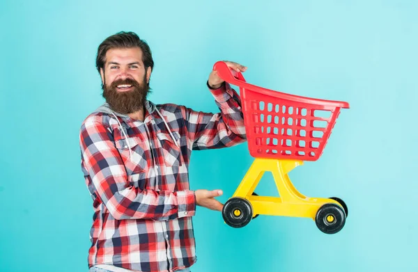 Havalı saç stili olan şık sakallı adam kareli gömlek giyer, alışveriş arabası satar. — Stok fotoğraf