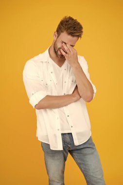 Korkunç bir baş ağrısı. Başı ağrıyan kot gömlekli yakışıklı bir adam. Yorgun ve stresli bir adam sarı arka planda. Stresli yaşam konsepti. Baş ağrısı, migren ve spazm. Sağlık sorunları. İş hayatı