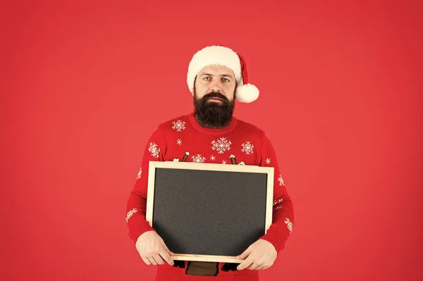 De man met de baard heeft een blanco schoolbord kopieerruimte. Guy Santa Claus rode achtergrond. Kerstman hoed met reclame. Krijtbord voor informatie. Winter aankondiging. Winter evenement. Wintervakantie — Stockfoto