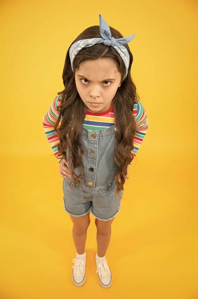 Ένα κακοδιάθετο παιδί. μικρό κορίτσι κίτρινο φόντο. κομμώτρια. Το θυμωμένο ρετρό παιδί φοράει πολύχρωμα ρούχα. casual denim μόδα. Καλοκαιρινές τάσεις αξεσουάρ. Είναι πολύ χαριτωμένη. — Φωτογραφία Αρχείου