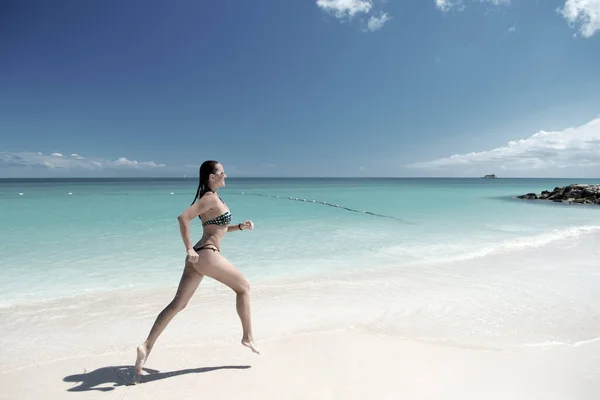 Ung kvinna som springer på den tropiska stranden — Stockfoto