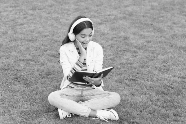 Conceito de educação e leitura. desenvolvimento da imaginação. bonito menina ler livro. menina pré-escolar feliz com livro no quintal da escola. de volta à escola. criança trabalhadora em fones de ouvido — Fotografia de Stock