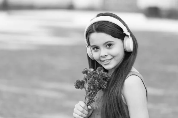 Muzyka dla uszu. Szczęśliwe dziecko z kwiatami słucha muzyki. Dziewczynka nosi słuchawki grające muzykę. Wakacje. Nowa technologia. Współczesne życie. Zabawa i rozrywka. Pozwól muzyce cię zabrać — Zdjęcie stockowe